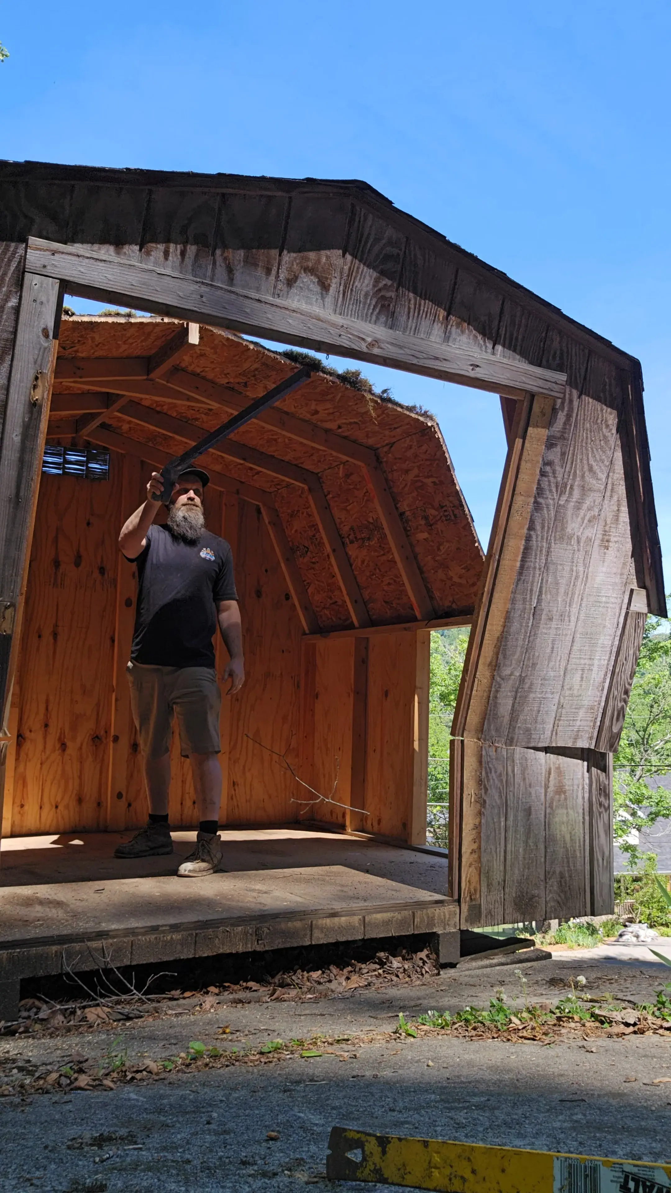 Kraken Junk Removal crew member using a pry bar to dismantle a wooden barn-style shed