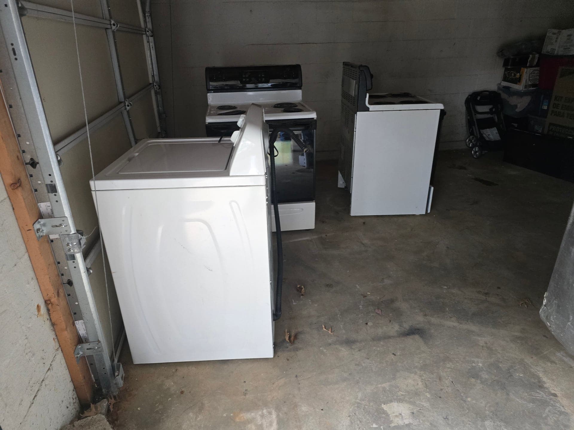 White washing machine and two electric ranges staged in a garage before appliance removal