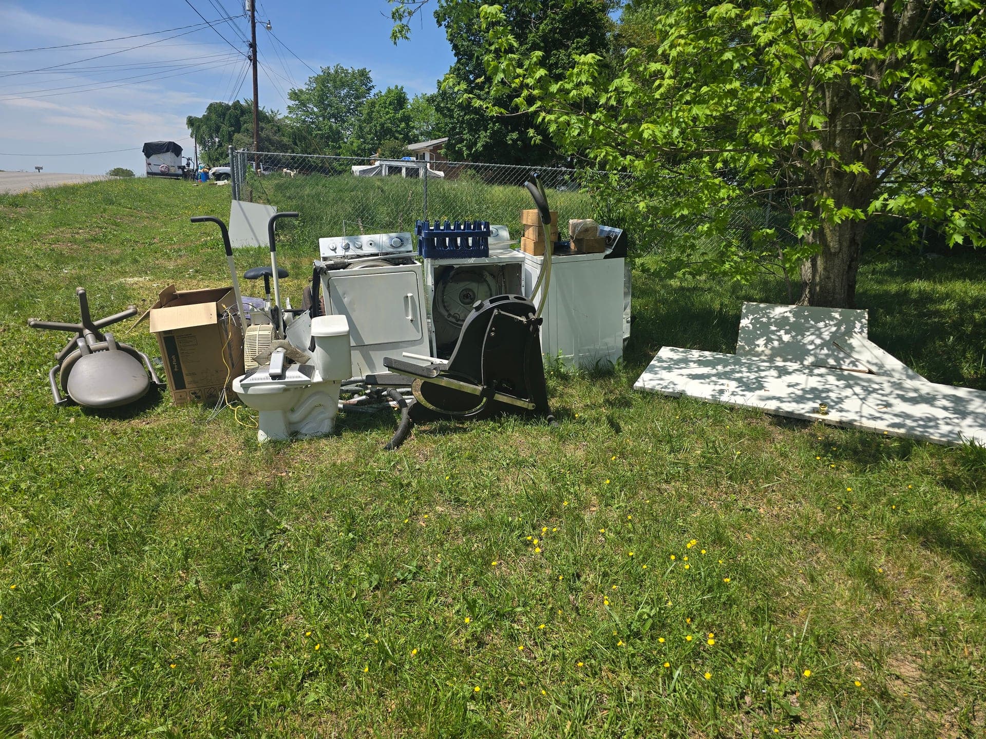 Pile of washers, dryers, and other bulky household items staged on a grassy lawn before bulk appliance removal