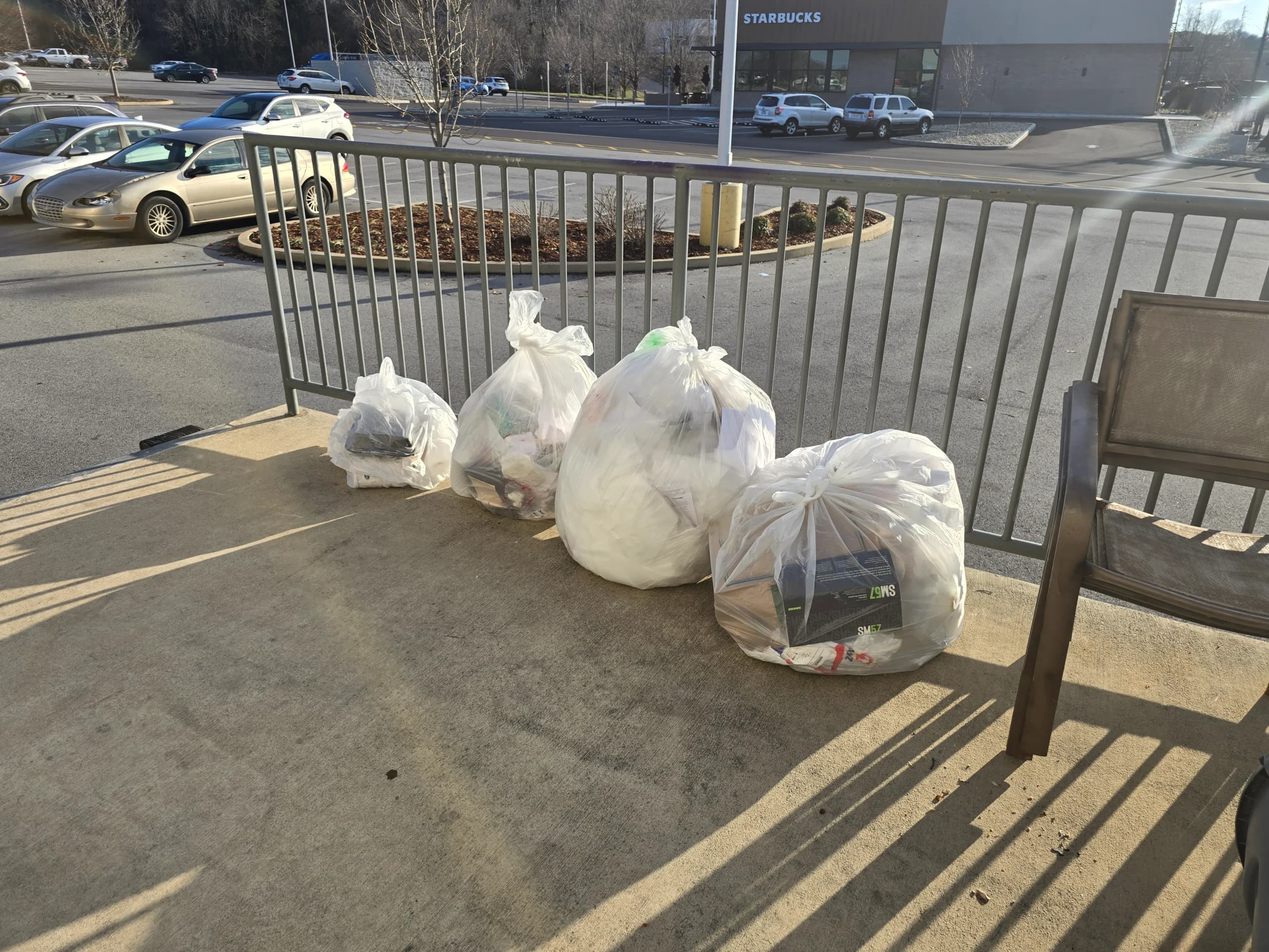 Four white trash bags lined up on a concrete walkway beside a metal railing in Johnson City, TN