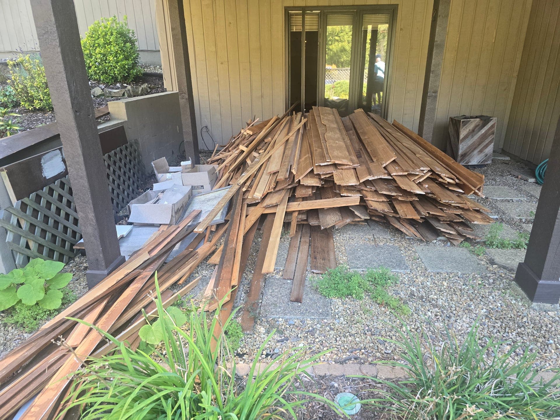Pile of wood planks and cardboard boxes of remodel scraps on a gravel patio under a covered area