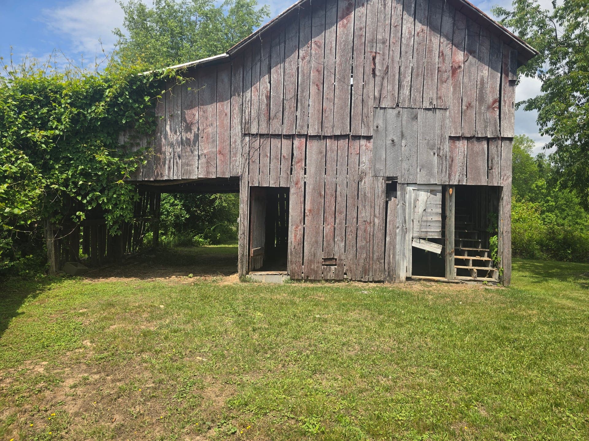 Same weathered wooden barn with the yard and open bays cleared after debris removal