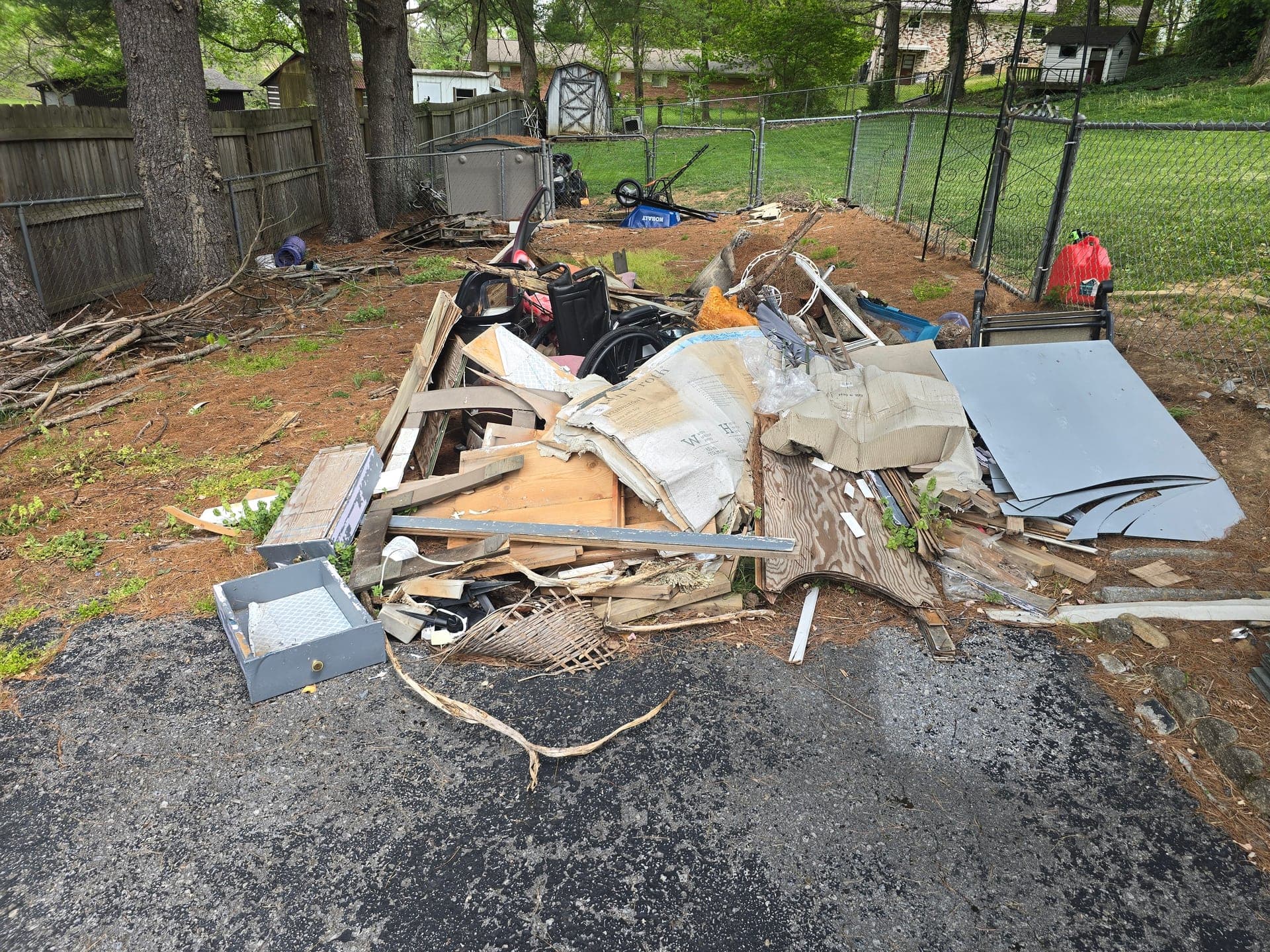 Backyard pile of plywood, lumber, cardboard, and mixed scrap beside fences before removal