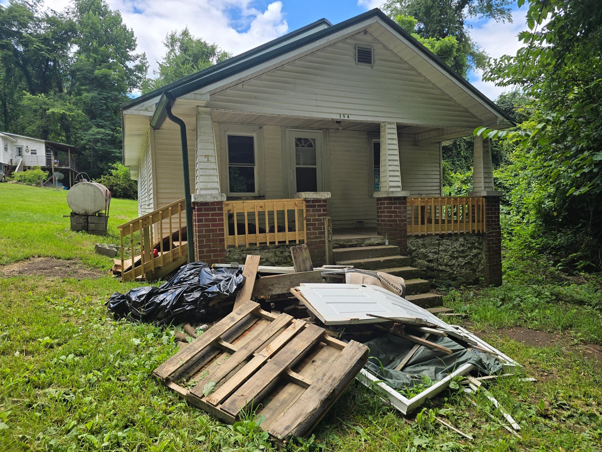 Pile of pallets, lumber, a white door, and remodel debris on the front lawn before a house porch