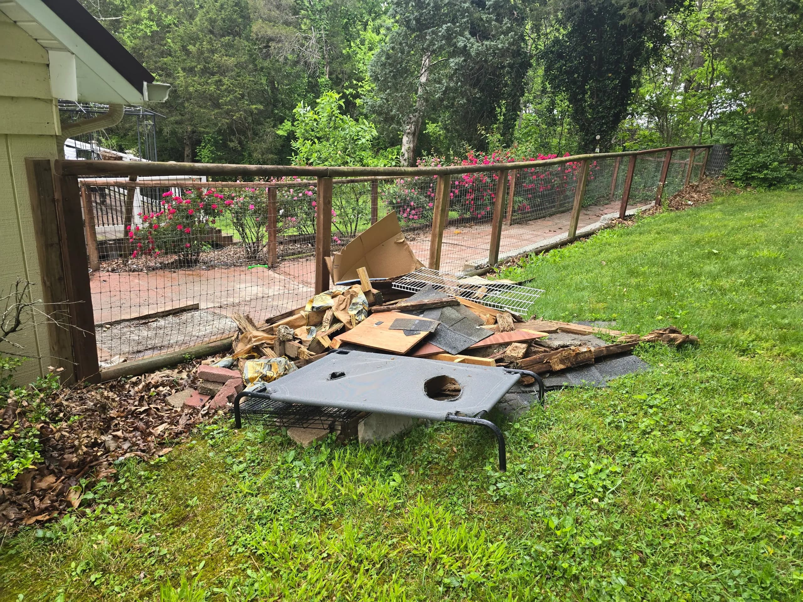 Backyard pile of cardboard and scrap wood beside a fence before construction debris removal by Kraken Junk Removal