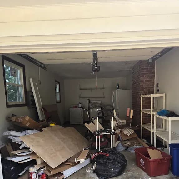 Garage packed with plywood, cardboard, and bagged debris before cleanout by Kraken Junk Removal