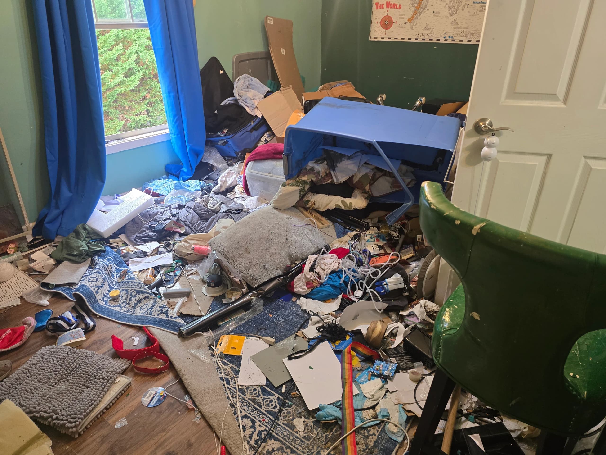 Bedroom floor covered with clothes, storage bins, bags, and household items beside a green chair