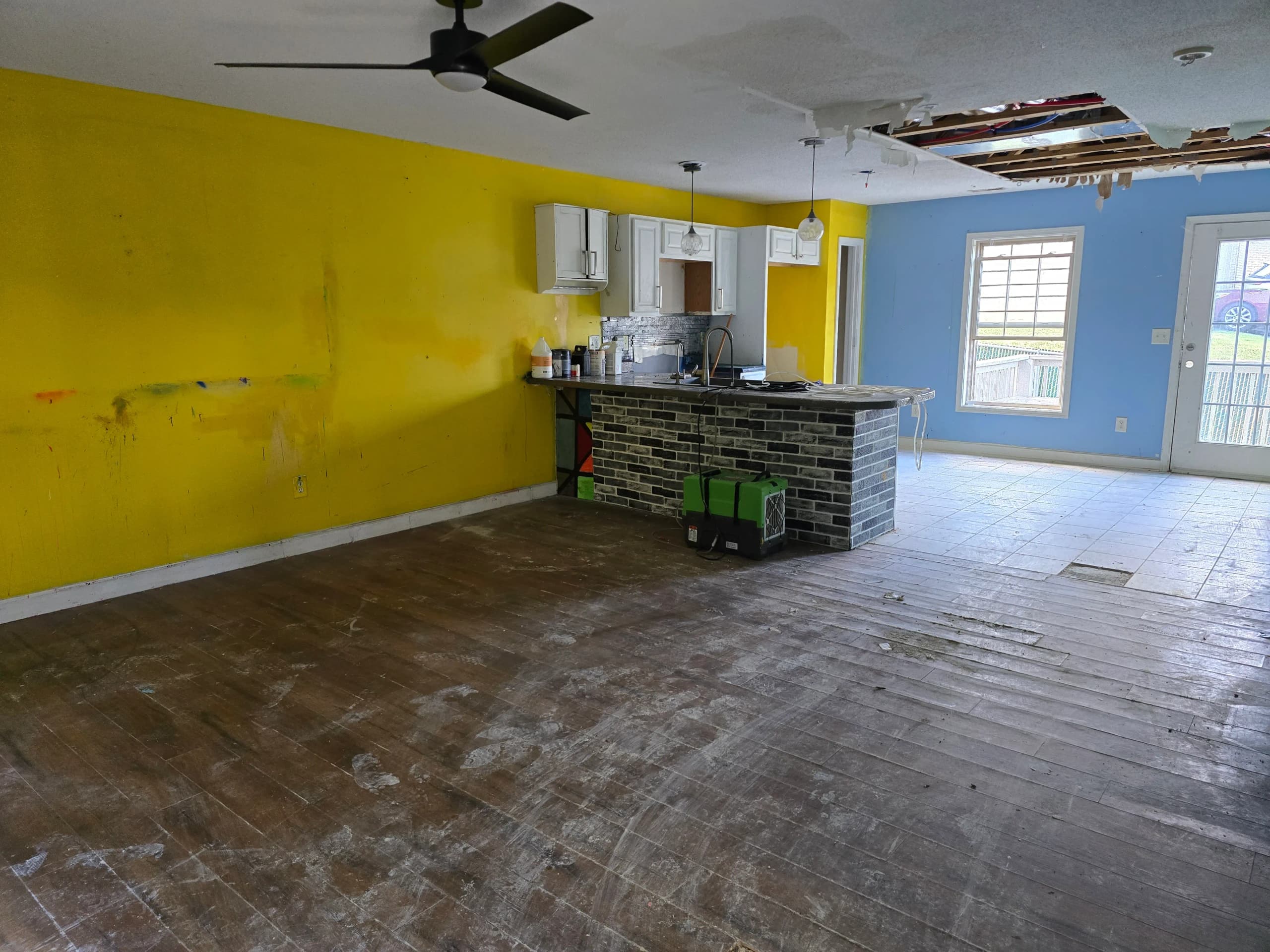 The same living room and kitchen after the furniture and clutter were removed, with the ceiling hole still open