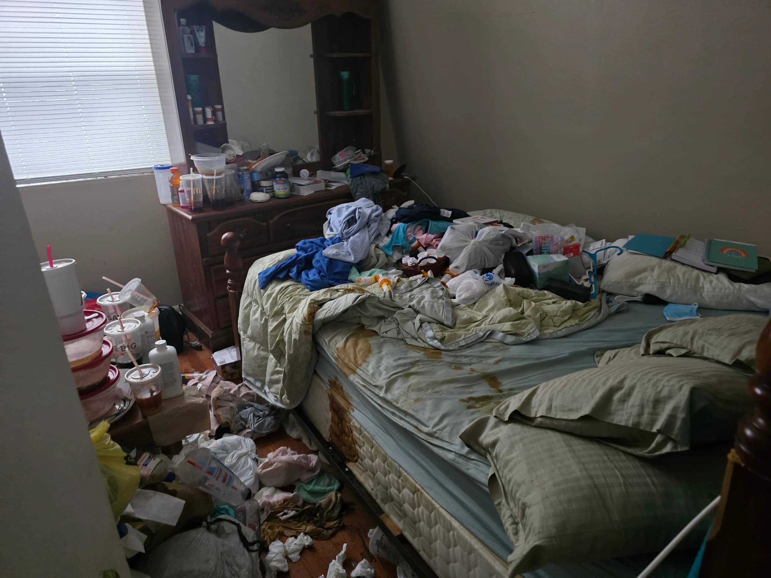 Bedroom with clothes, bedding, and household items covering the bed, dresser, and floor