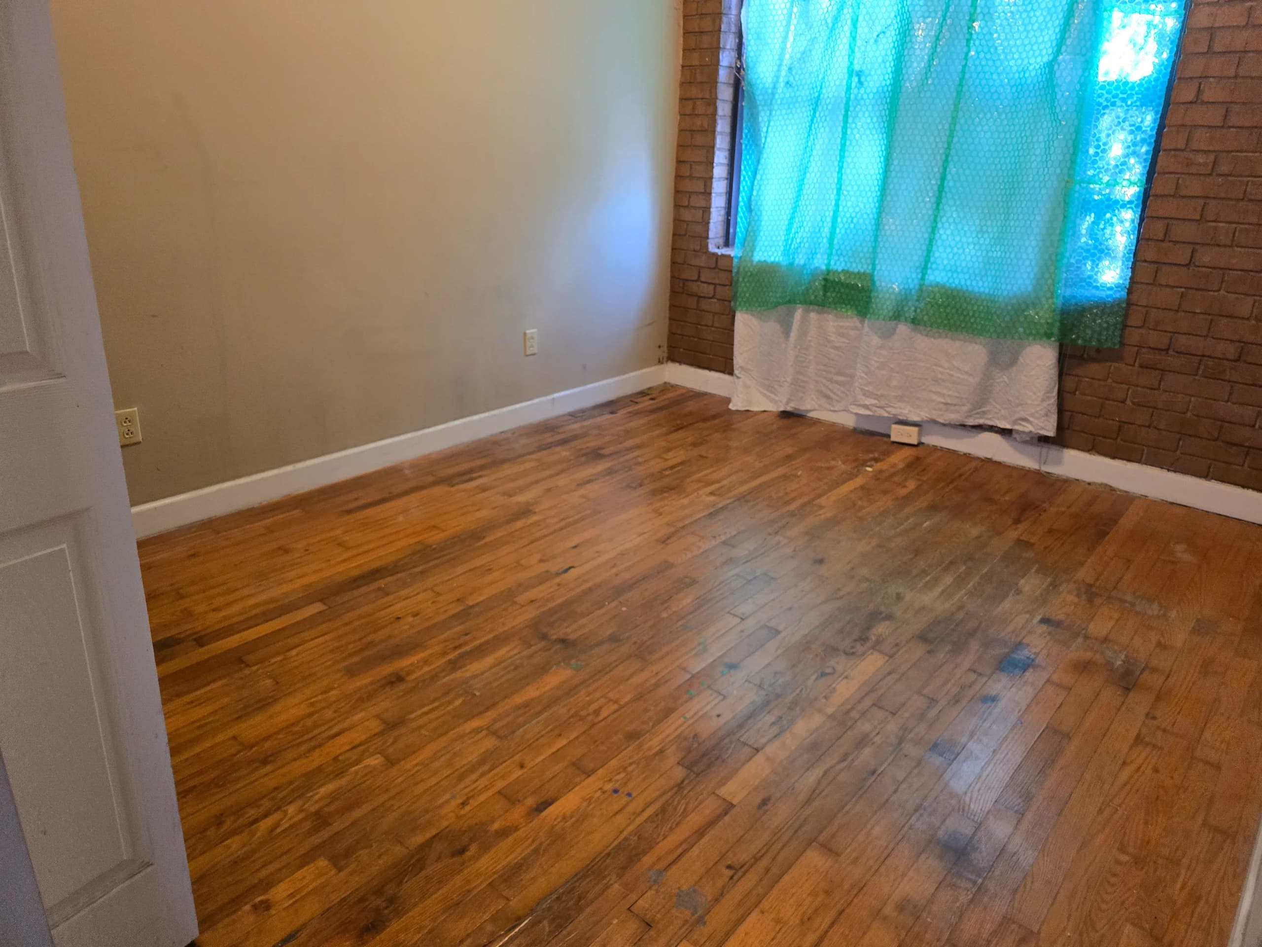 Empty room with hardwood floors and a brick wall after a house cleanout