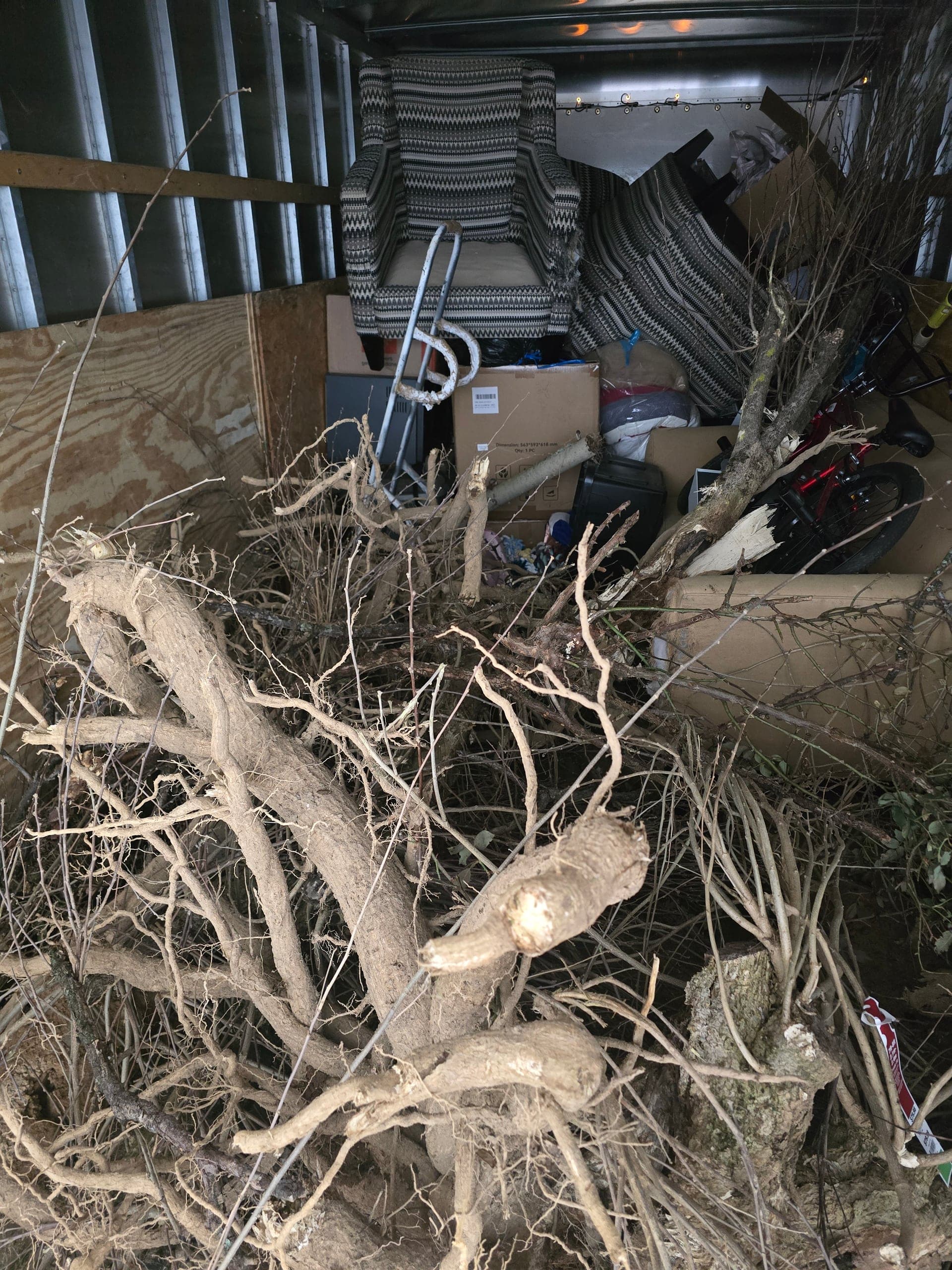 Truck load of tree roots and branches in front, with armchairs, boxes, and a bicycle loaded behind