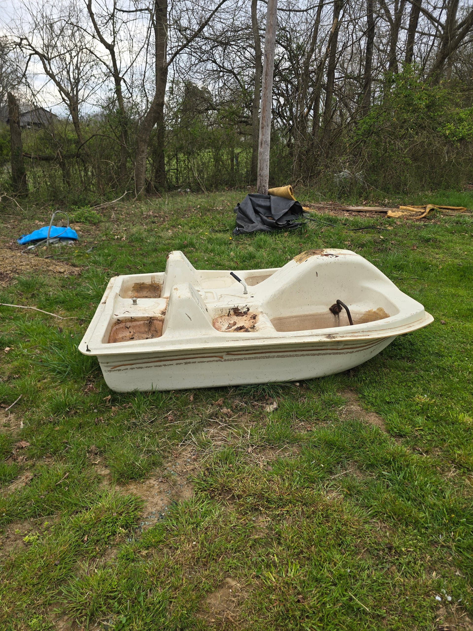 Weathered paddle boat sitting on a lawn with leaves and dirt in its footwells