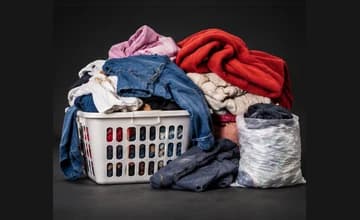 Laundry basket of clothes, folded blankets, jeans, and a bag of clothing