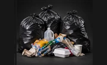 Tied black trash bags with loose bottles, containers, and food packaging