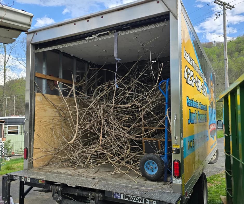 Kraken Junk Removal truck loaded with a large pile of dry branches and brush from a yard waste removal job