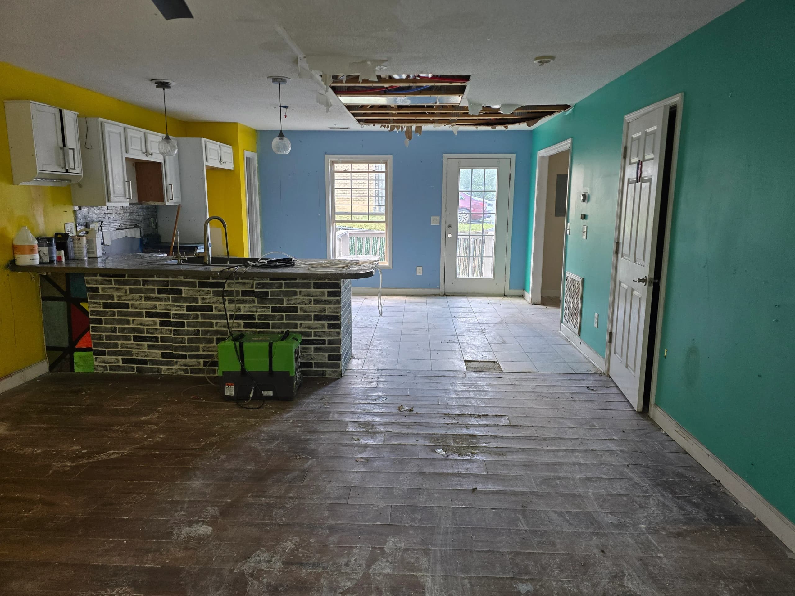 The same kitchen after the piled contents were removed, with the ceiling hole still open and a dehumidifier beside the island