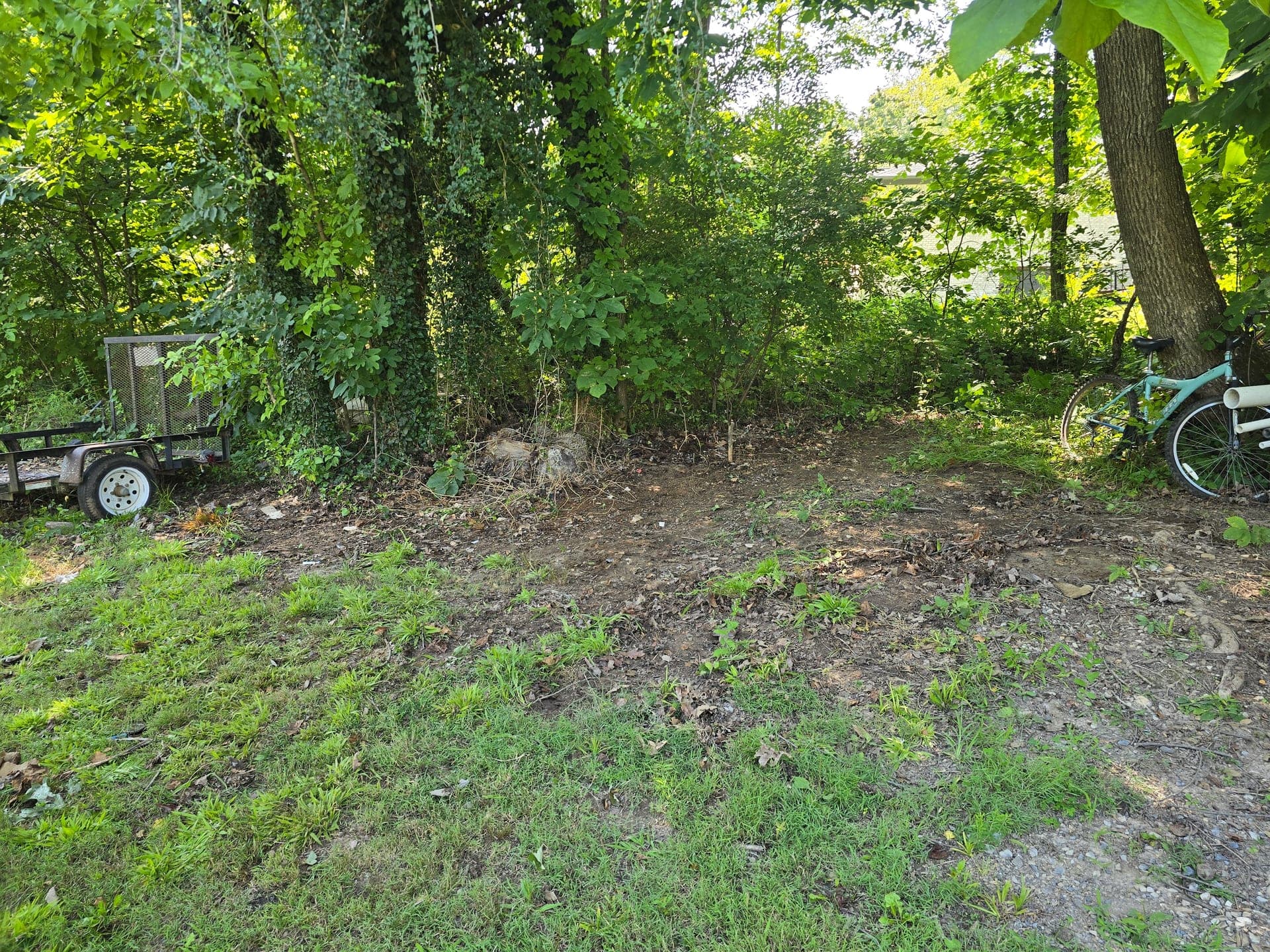 Cleared dirt and grass at the edge of a wooded lot after water heater removal