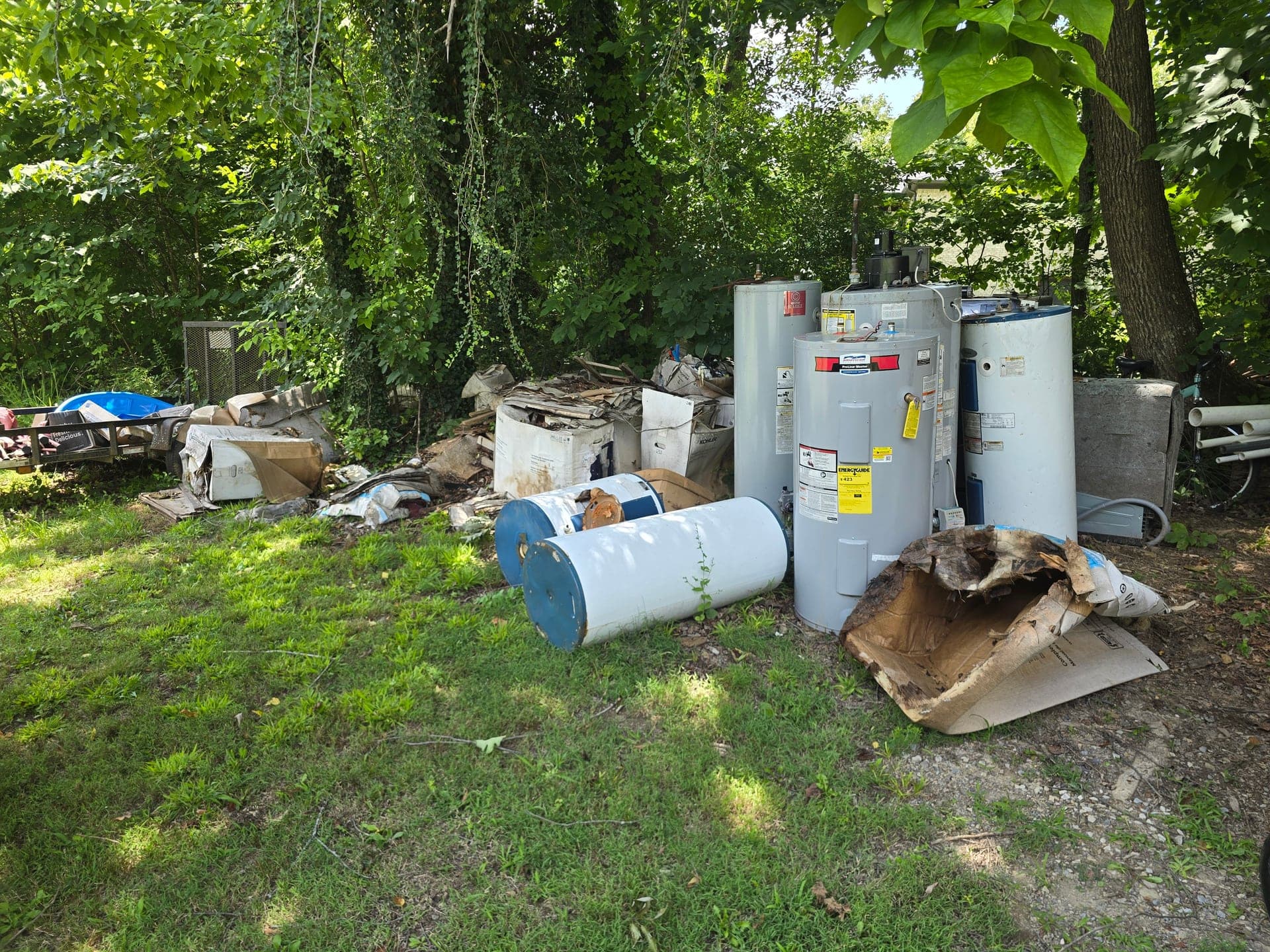 Several old water heaters and cardboard debris staged on grass before water heater removal