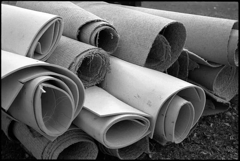 Rolls of pulled-up carpet and padding stacked outdoors