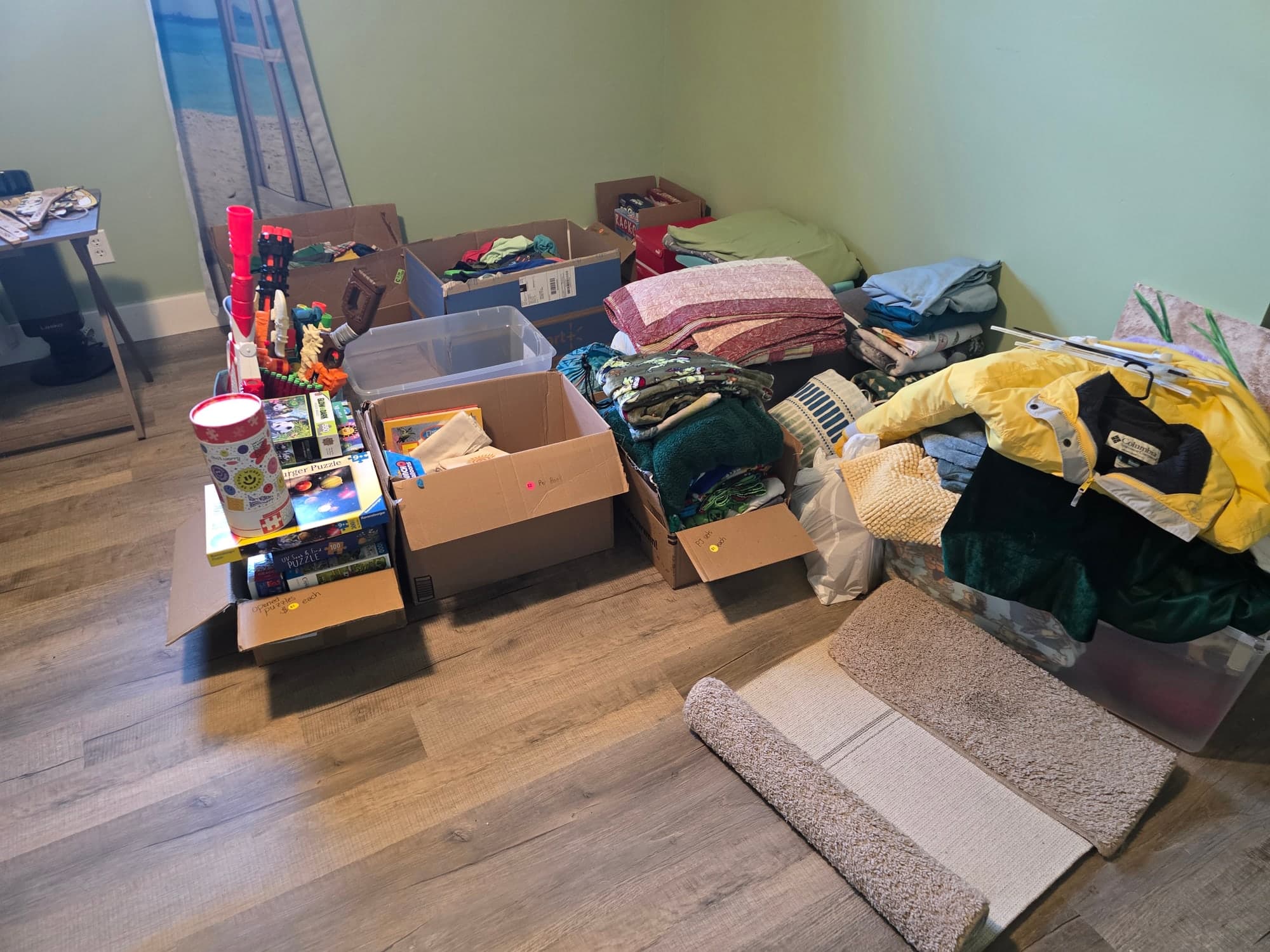 Cluttered bedroom with clothes, boxes, and belongings piled on a bed and floor before an estate cleanout