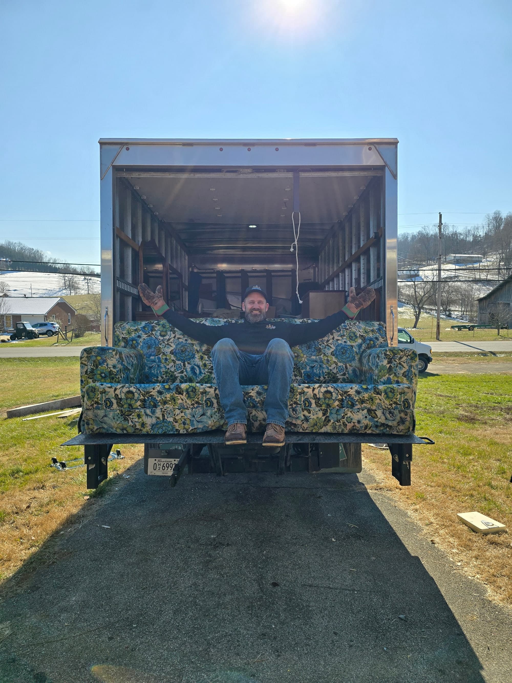 Kraken Junk Removal owner on a floral sofa loaded on the truck liftgate in Johnson City, TN