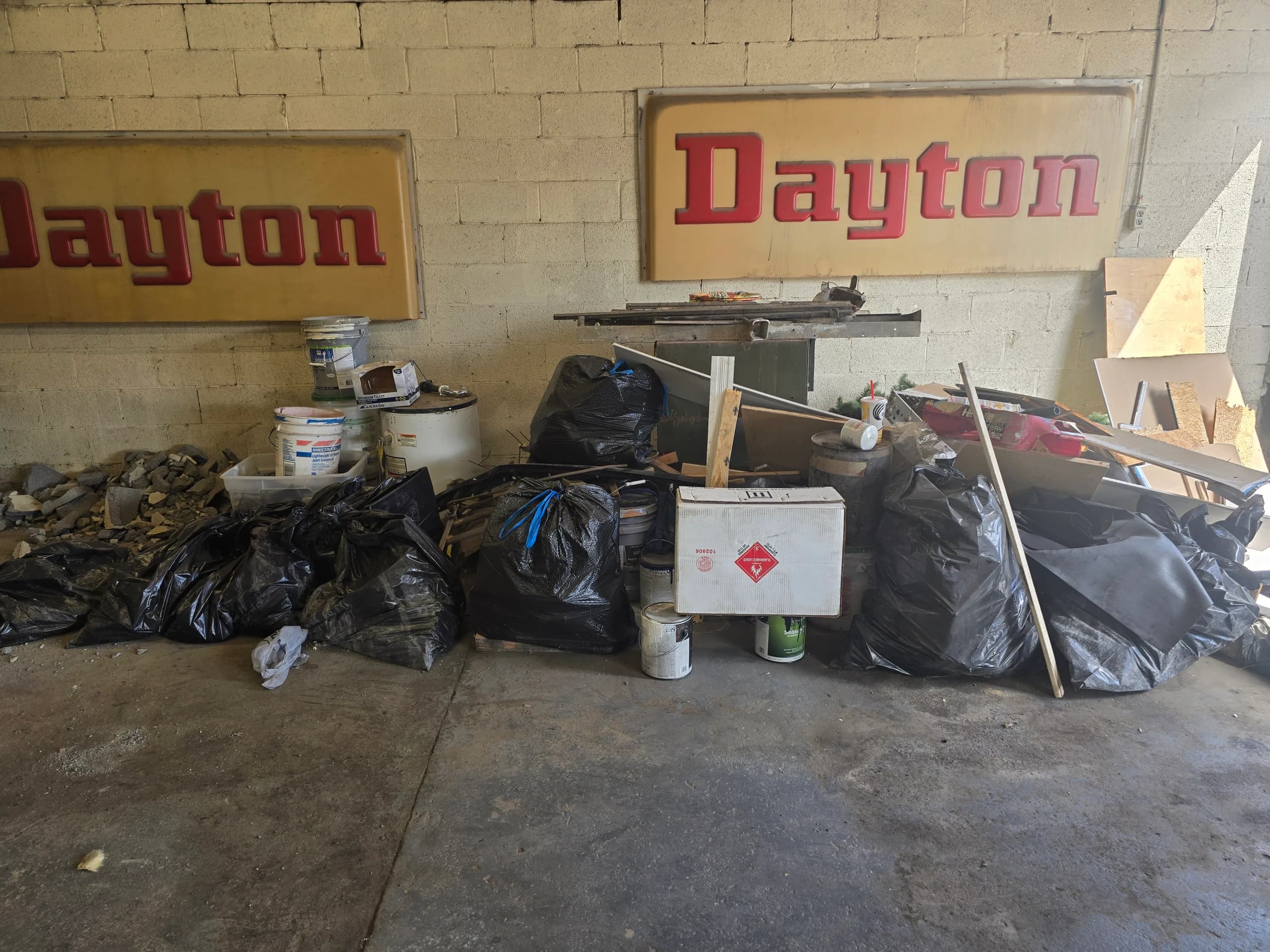 Bagged debris and buckets along a concrete block wall before garage cleanout by Kraken Junk Removal
